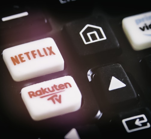 A close-up of a remote control featuring buttons for various streaming services, including Netflix and Rakuten TV, along with other navigational buttons.